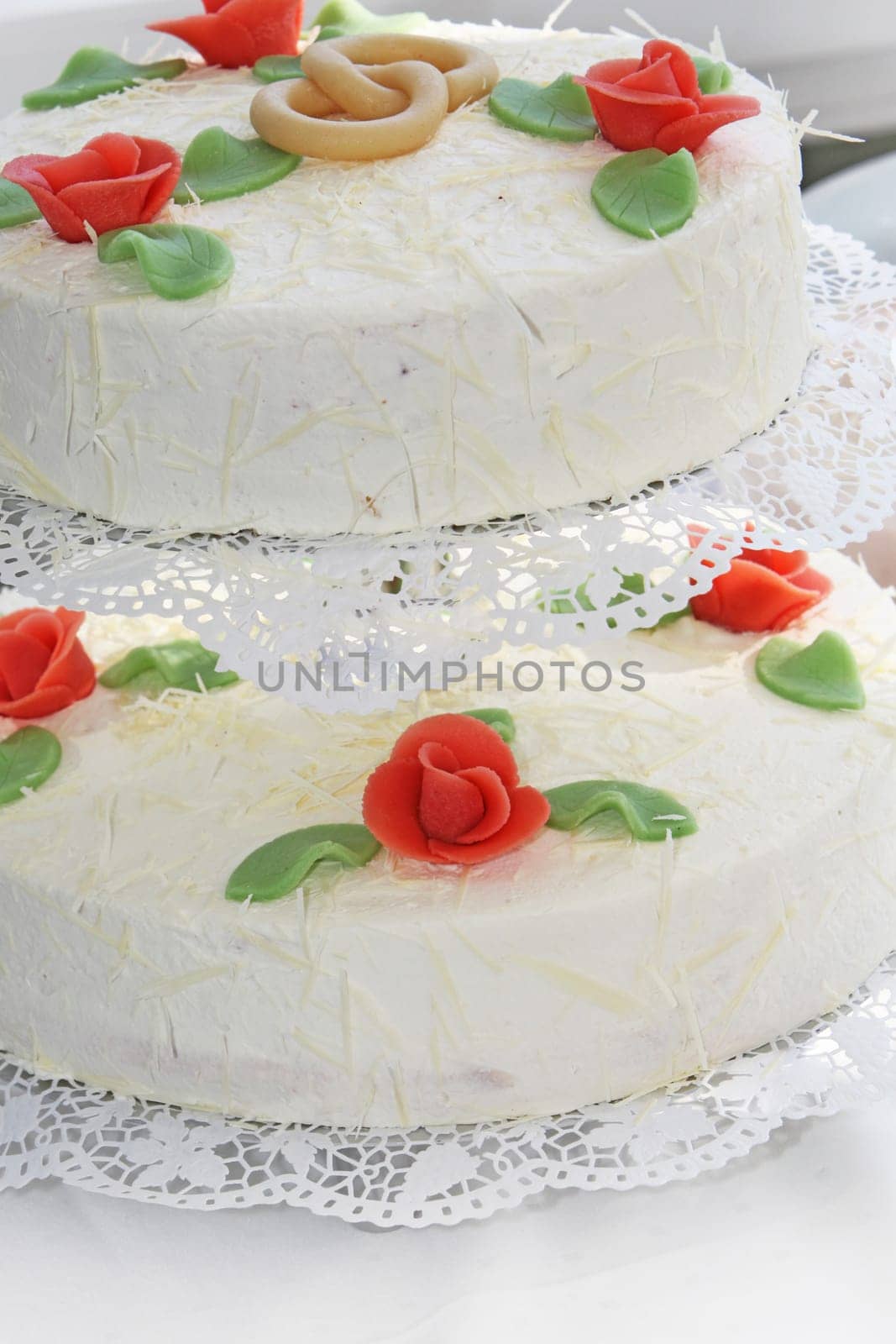 Two-layered wedding cake decorated with orangey red rose buds and intertwined wedding rings.