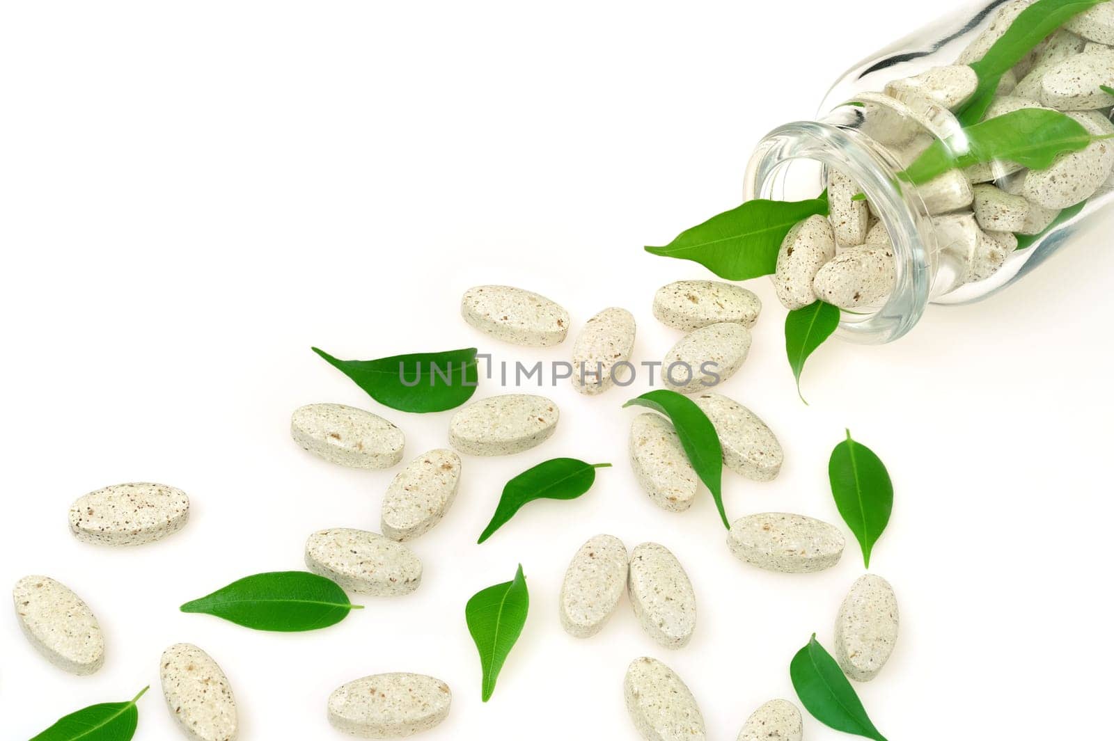 Herbal supplement pills and fresh leaves spilling out of bottle - alternative medicine concept