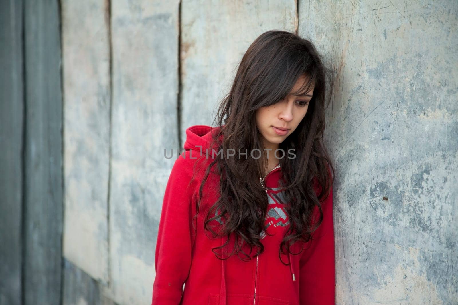Teenage girl leaning against grunge wall with expression of sadness.