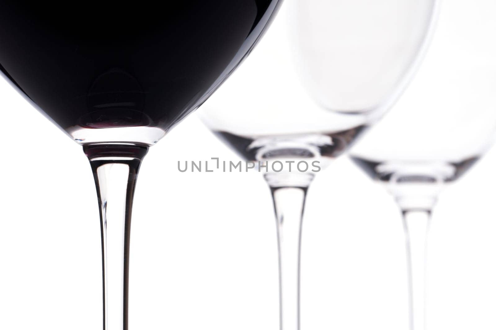 Three Bordeaux wine glasses backlit,one of which includes red wine from the Merlot grape variety