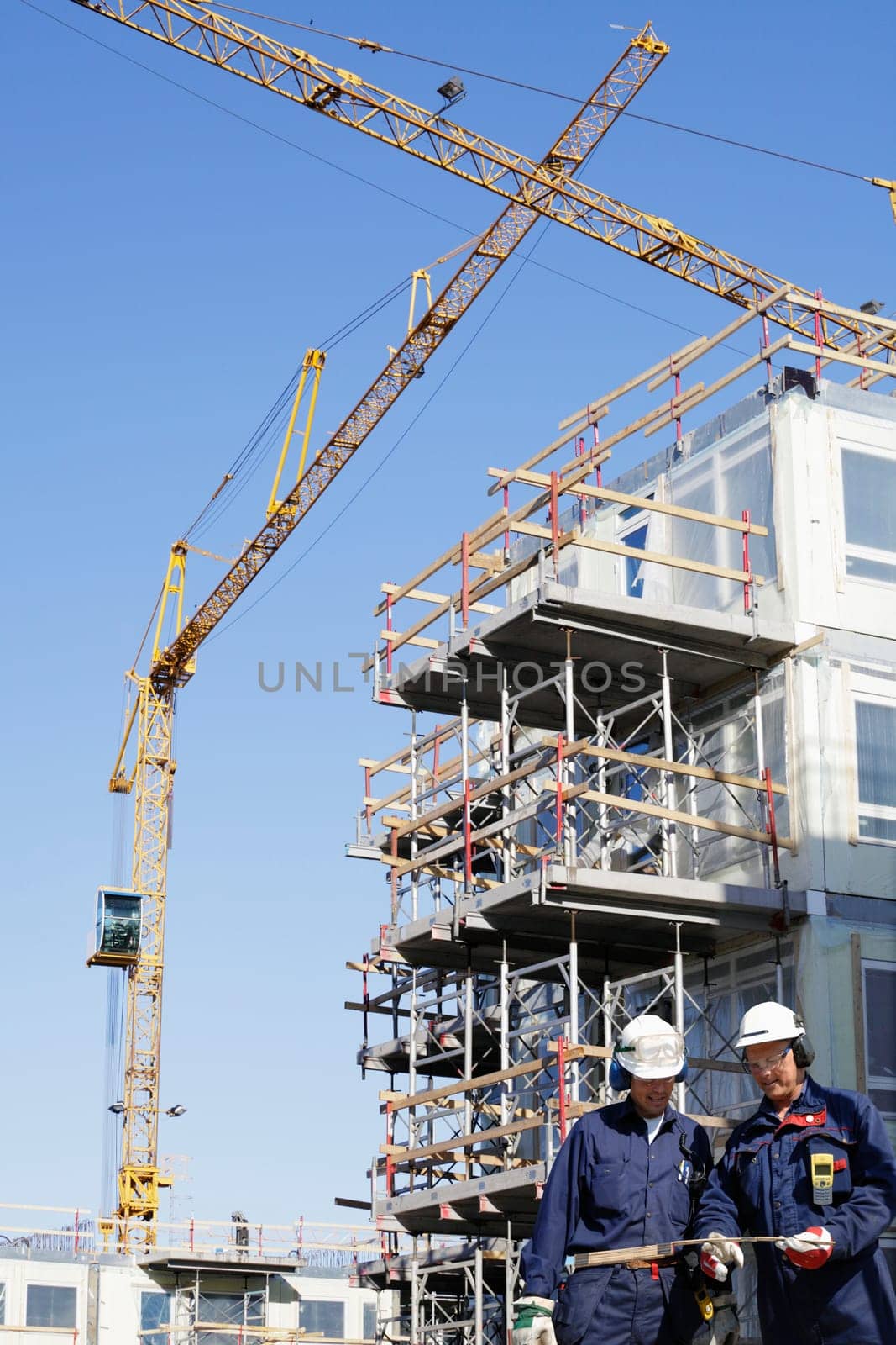 two construction workers with building site, cranes and scaffolding