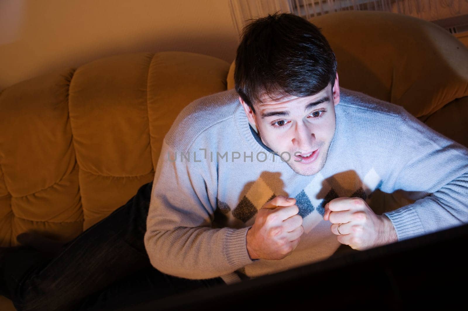 Young man with short brown hair lying tensely on the sofa in front of the TV