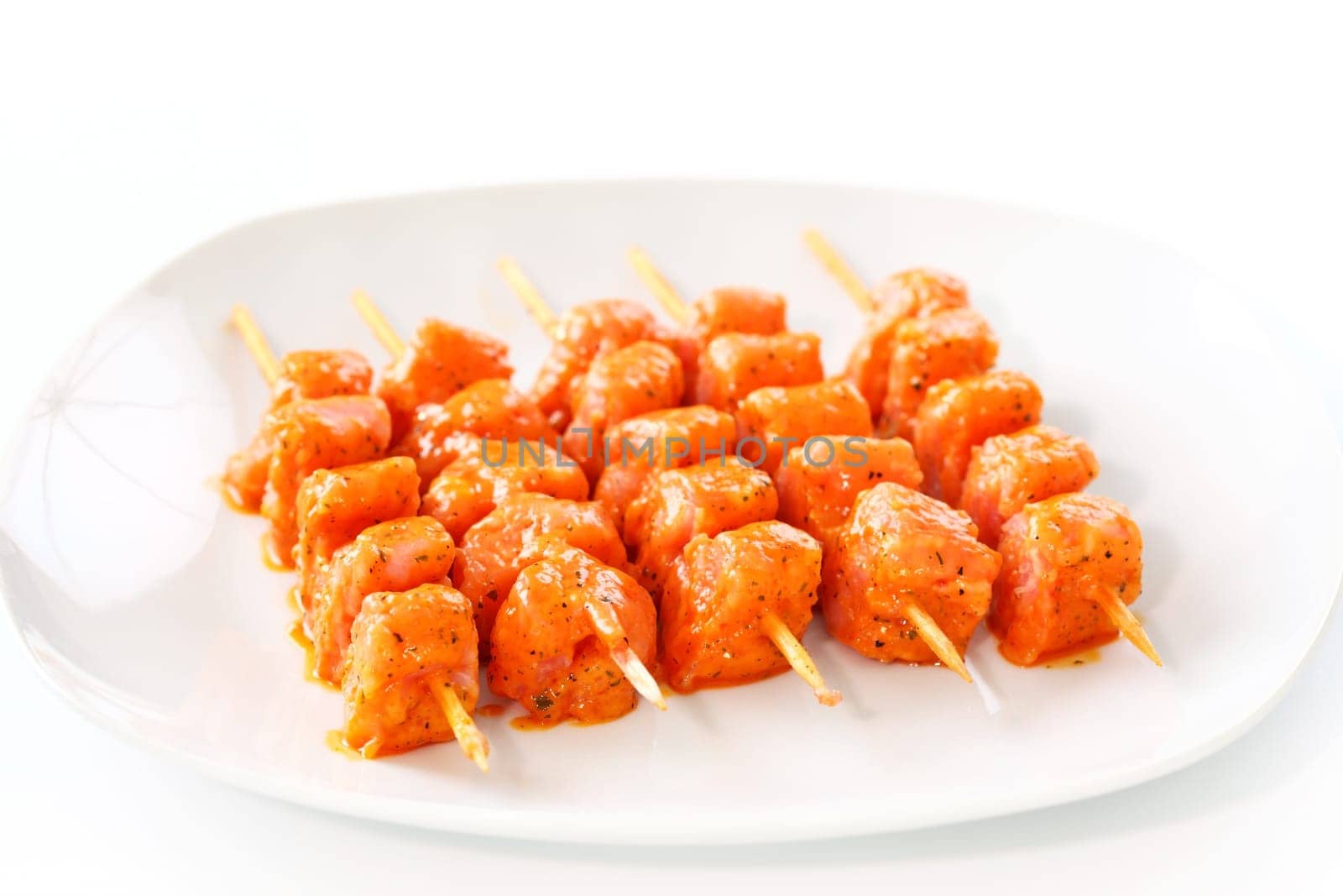 Raw skewered marinated chicken on white plate