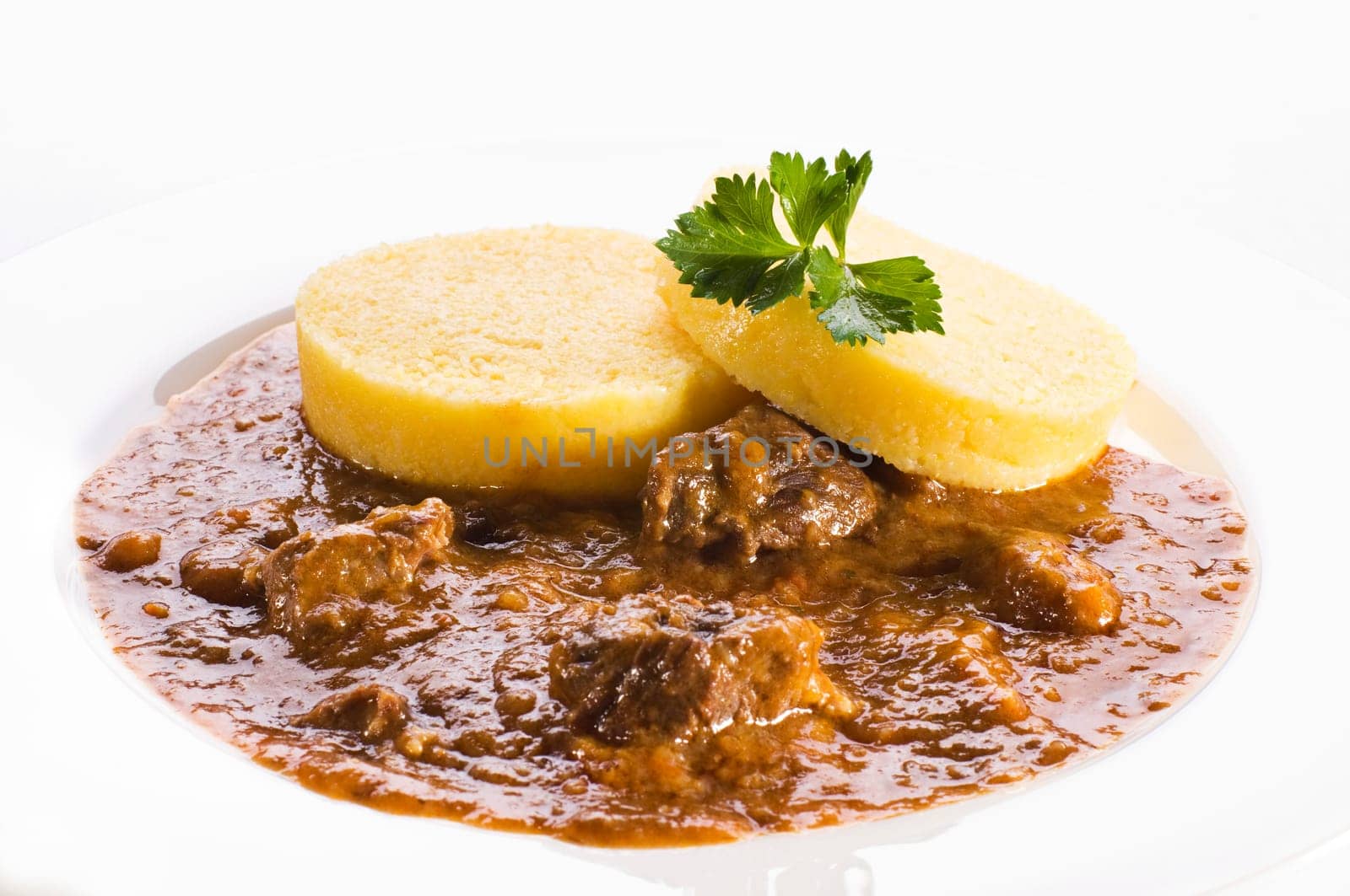 Fresh goulash with polenta on white plate close up