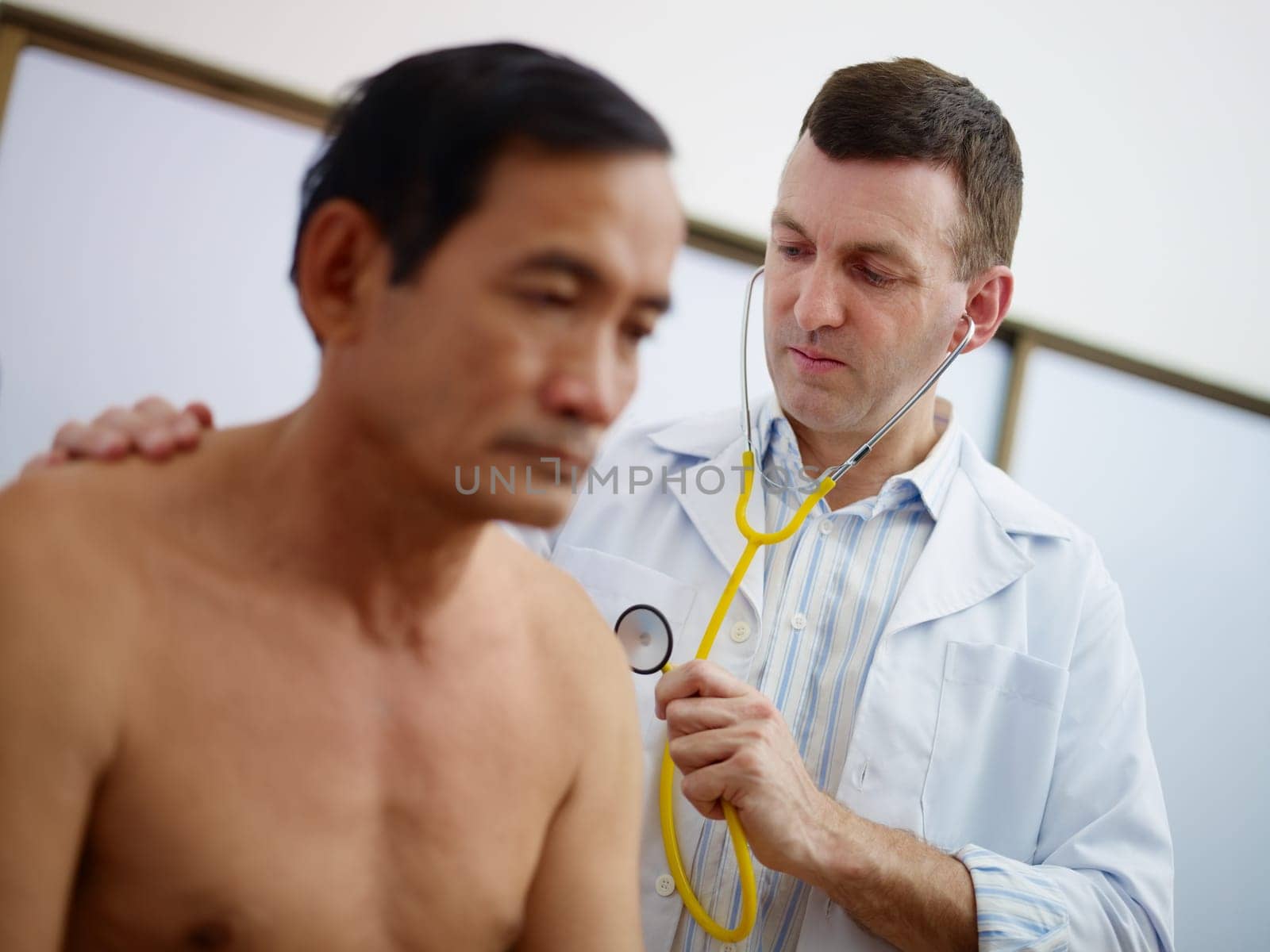 caucasian doctor working and visiting old asian male patient in hospital with stethoscope