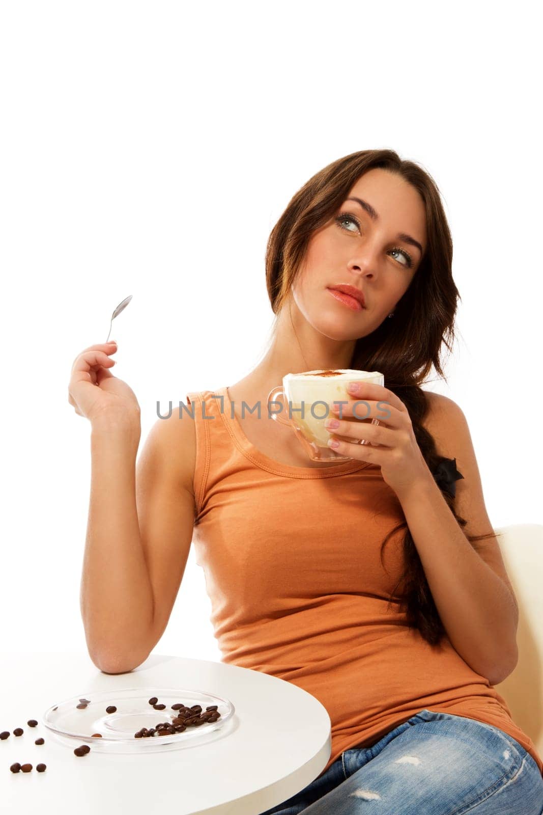 Young dreaming woman with a cup of cappuccino coffee sitting at a table against white background