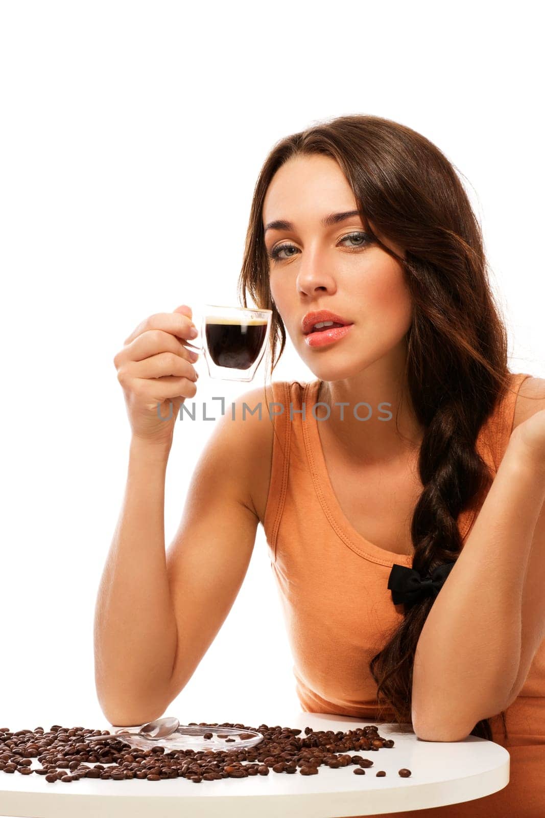 Beautiful young woman sitting at a table with a cup of espresso coffee against white background