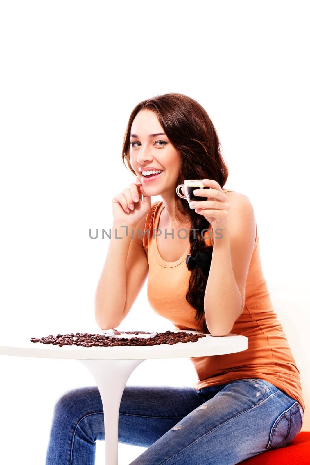 Laughing young woman sitting at a table with a cup of espresso coffee against white background