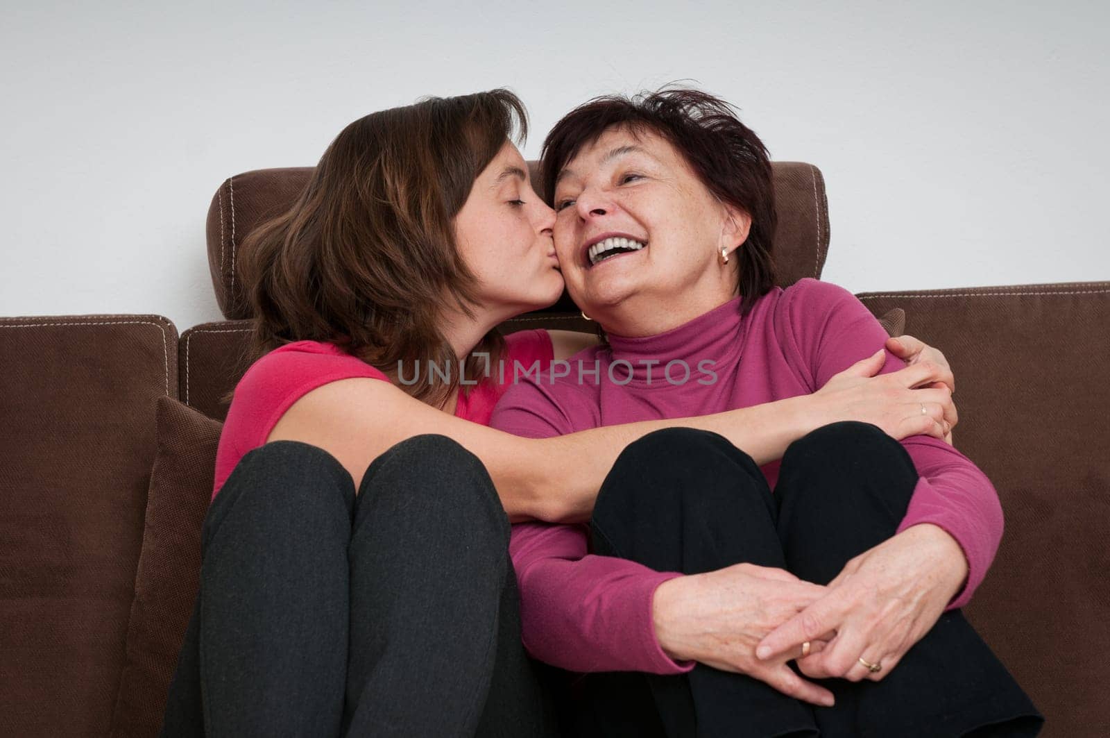 Portrait of daughter kissing happy senior mother sitting on sofa at home
