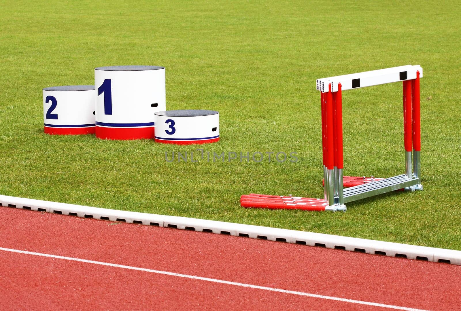 Track lanes with winner&#039 s podium and hurdles on green grass