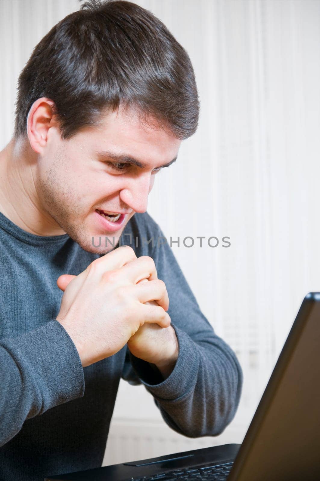Side upper body shot of a young man sitting at a laptop with mischievous and aggressive facial expressions and gestures