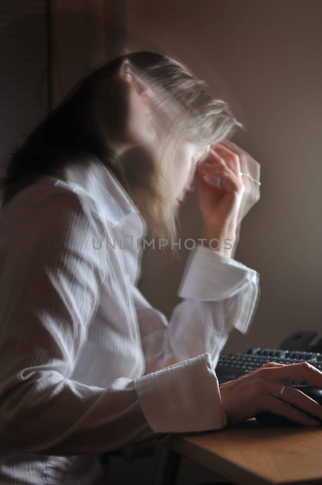 Young unhappy business woman working overtime at computer, night setting, motion blurr