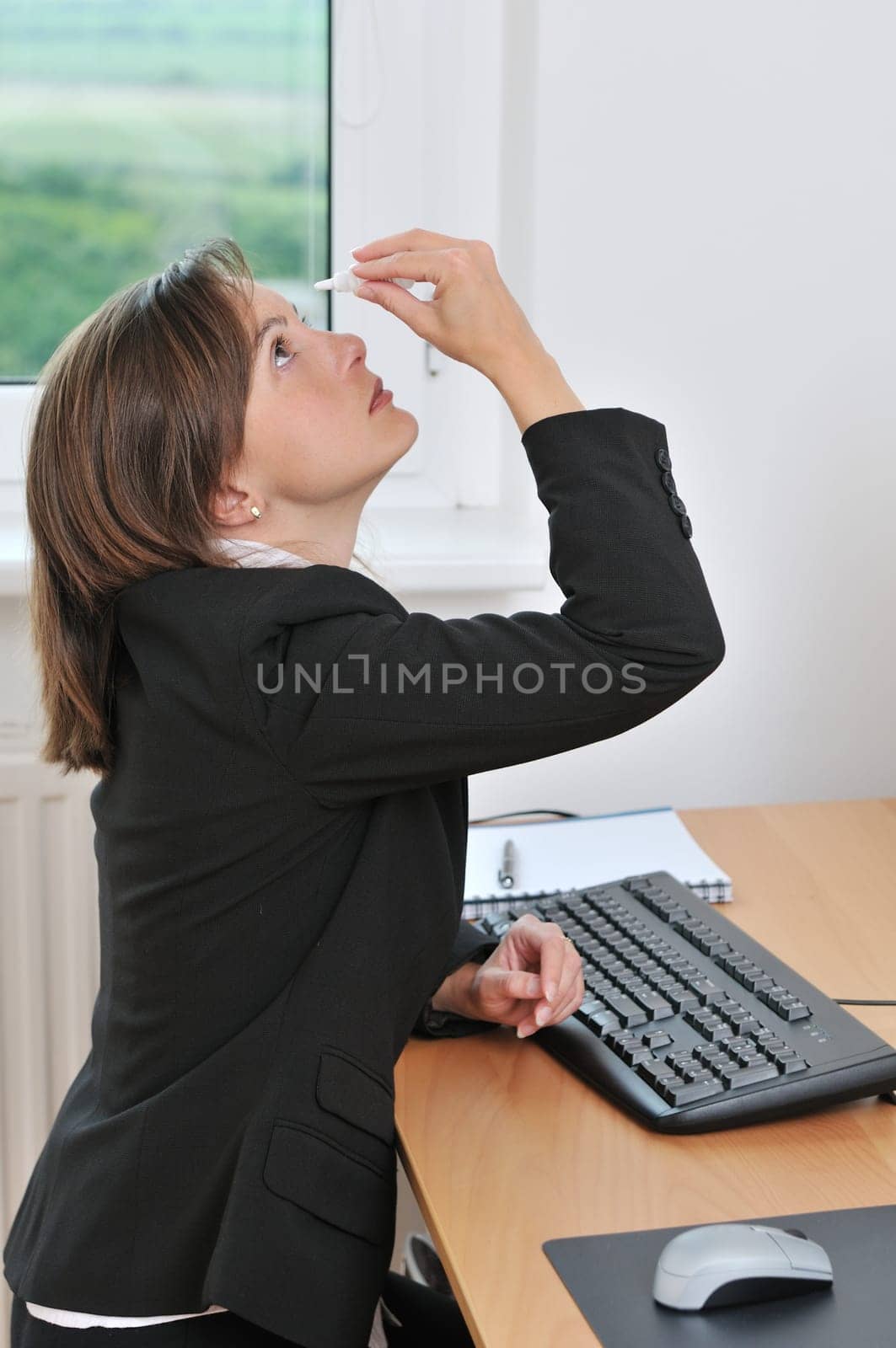 Detail of young business woman applying eye drops on workplace window in background