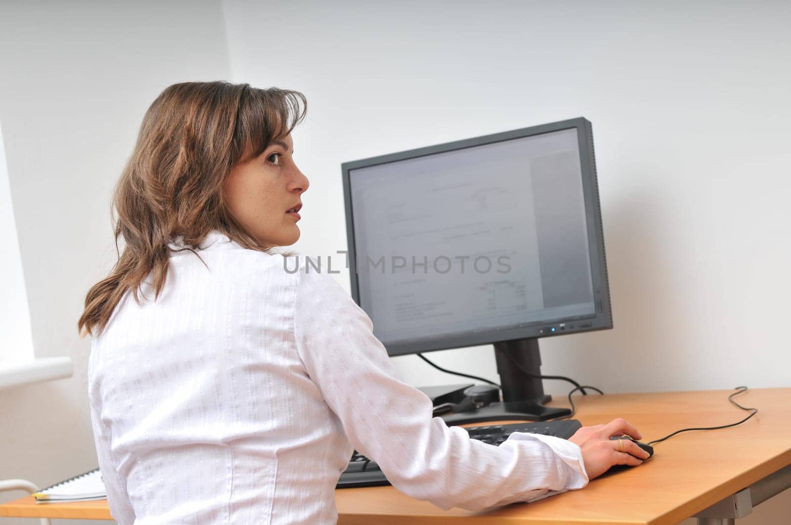Business person works at table with computer and looks over shoulder who is coming