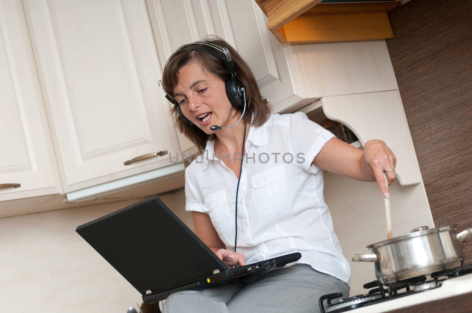 Young business woman having work conference call from home while cooking meal in kitchen