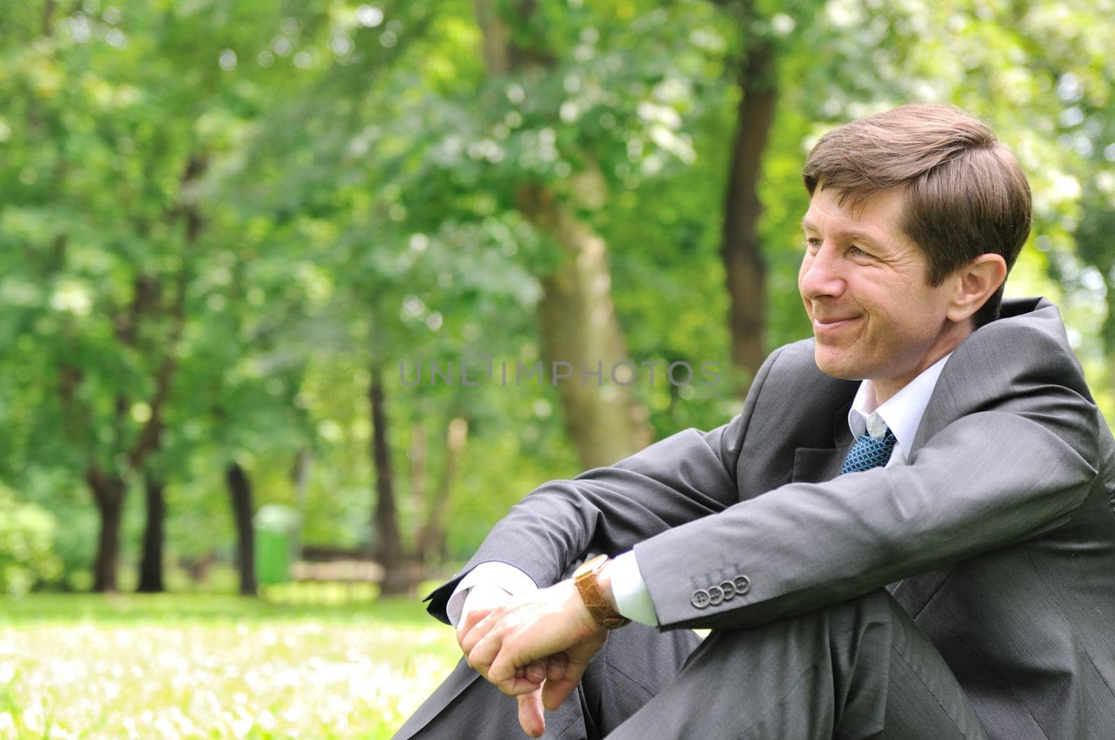 Senior people series - smiling mature business man siting on green grass and relaxing in park