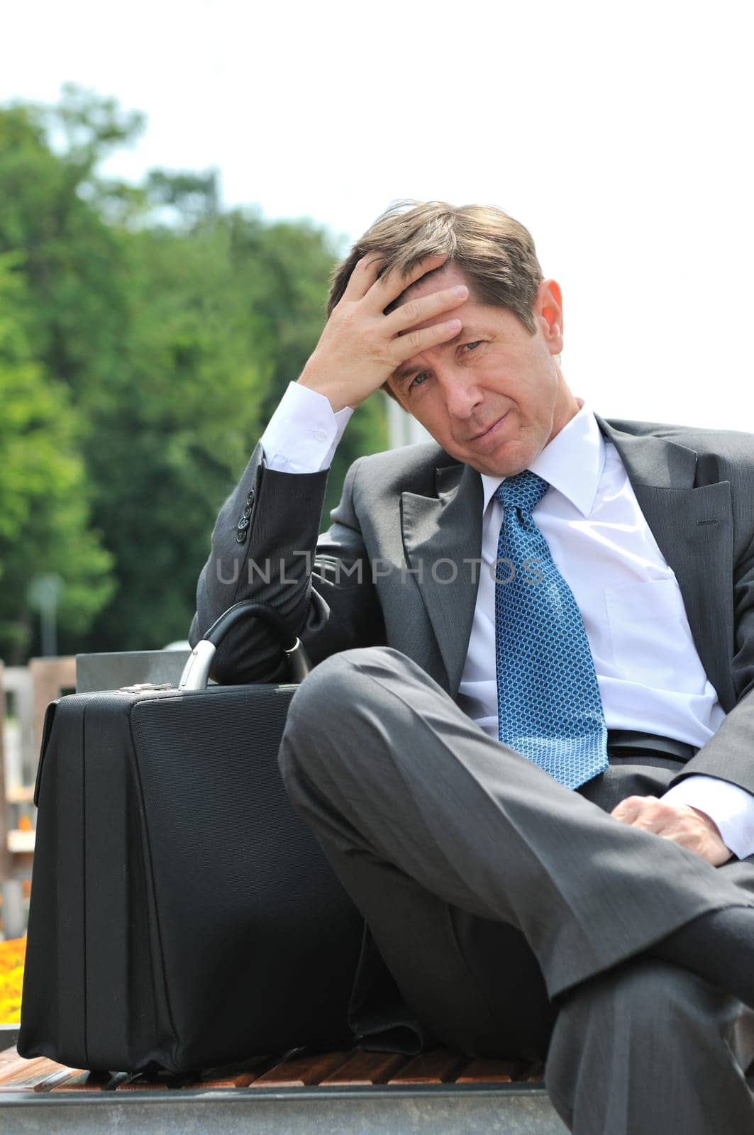 Portrait of depressed and worried senior business man siting on bench outdoors