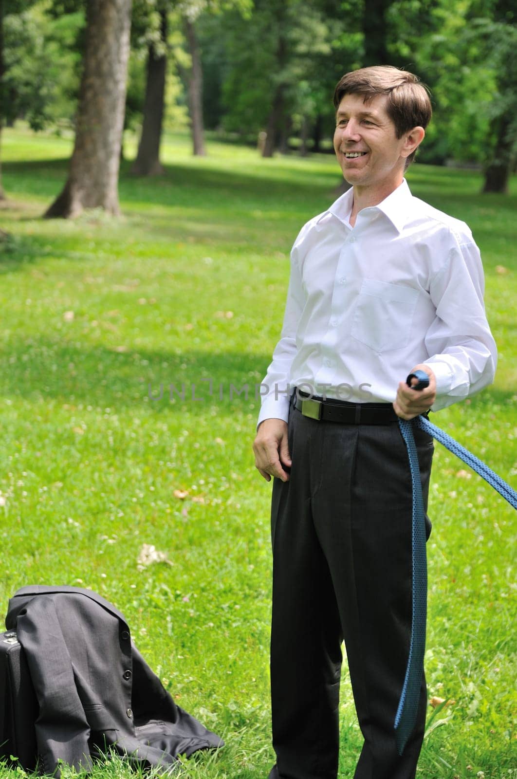 Escape from civilization - smiling senior business man putting off tie and relaxing in fresh green park