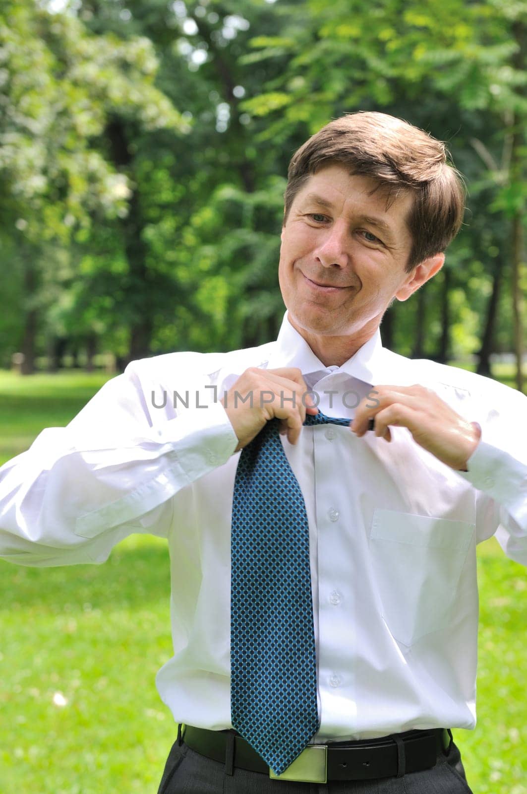 Escape from civilization - senior business man loosening tie in fresh green park