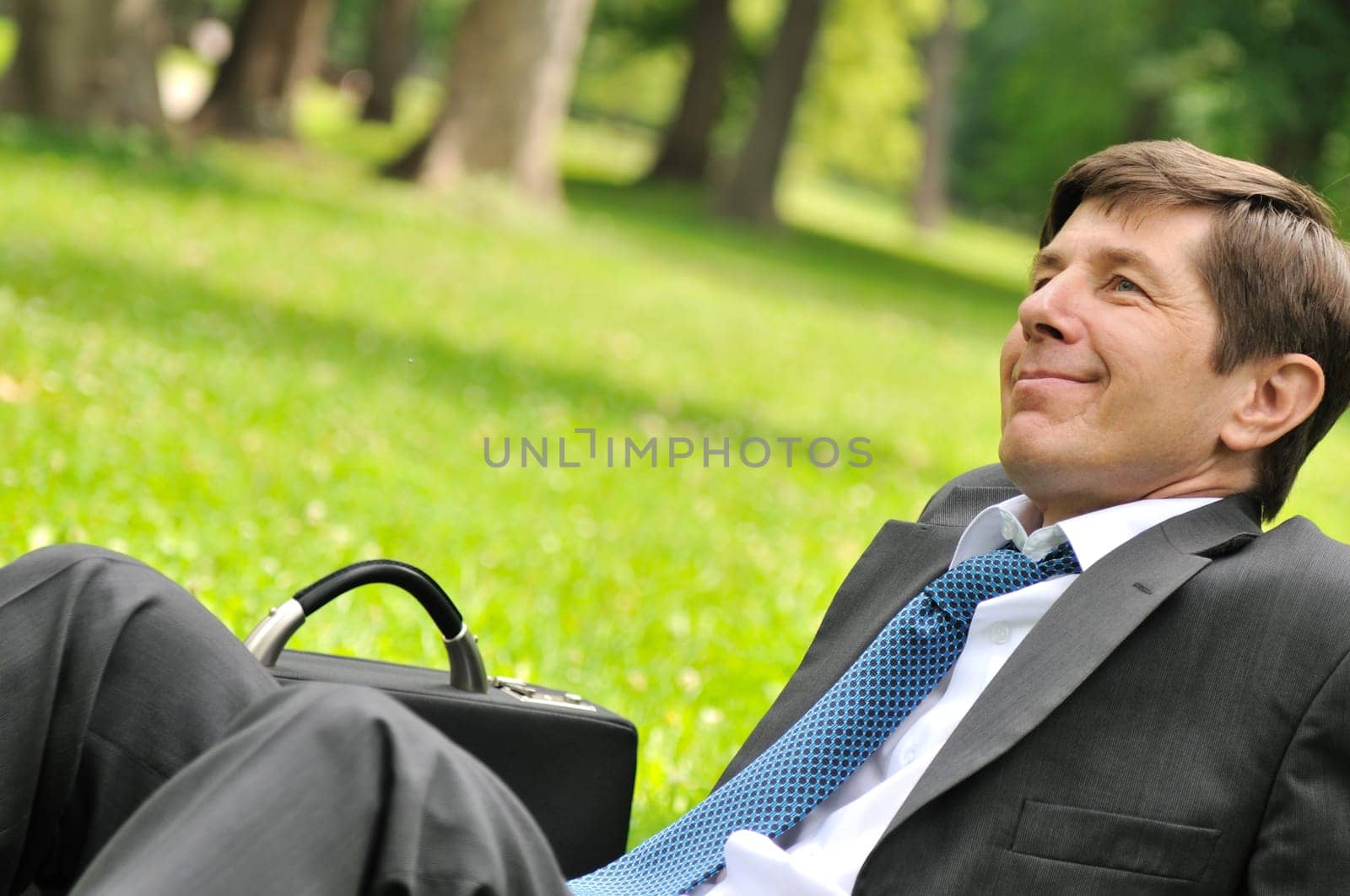 Senior people series - detail of cheerful mature business man siting on grass and relaxing in park