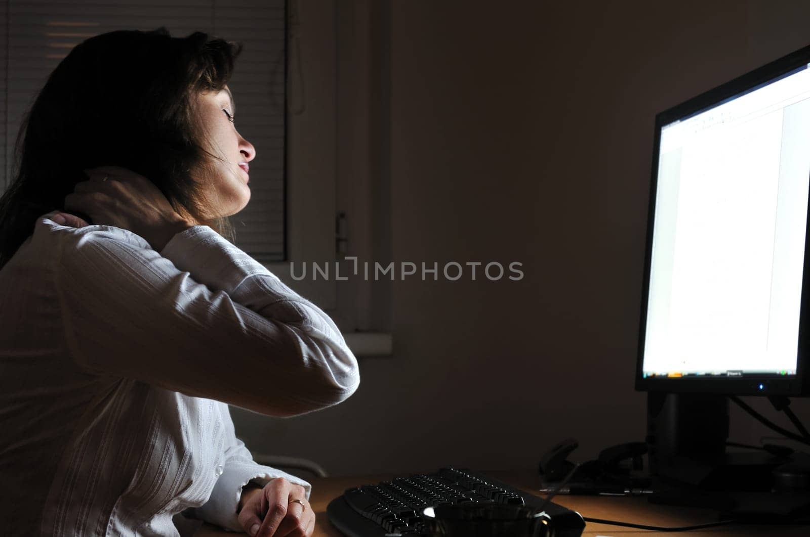 Neck pain - young tired business woman working overtime at computer, night setting