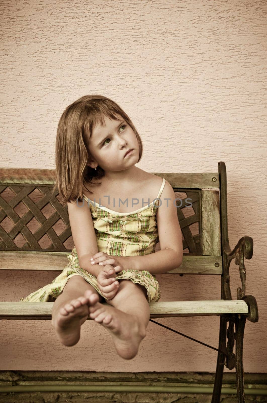 Portrait of cute child sitting on bench and stretching barefoot legs