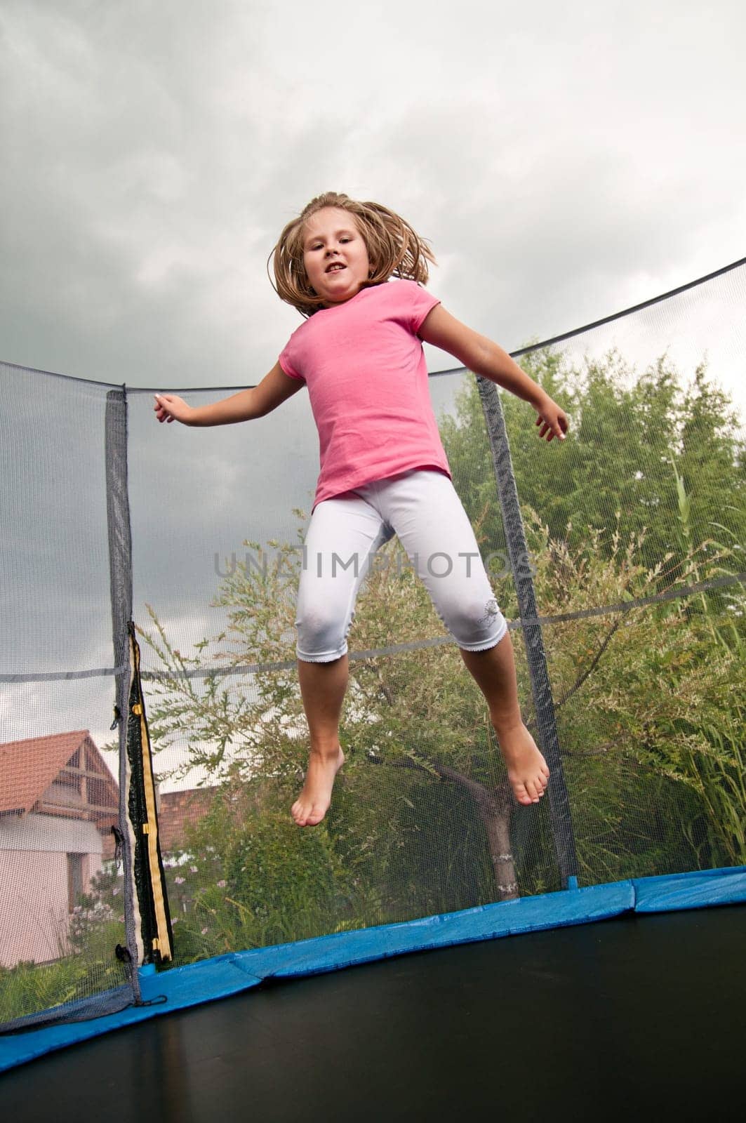 Small cute child jumping on trampoline - garden and family house in background