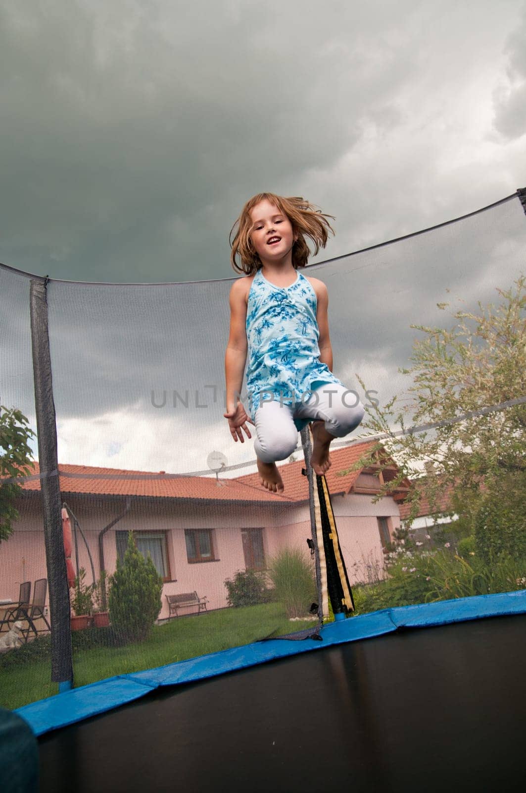 Small cute child jumping on trampoline - garden and family house in background