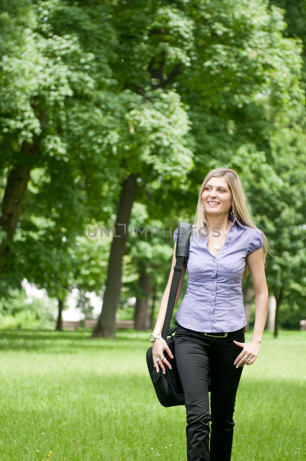 Young business woman wit laptob bag walking outdoors in park