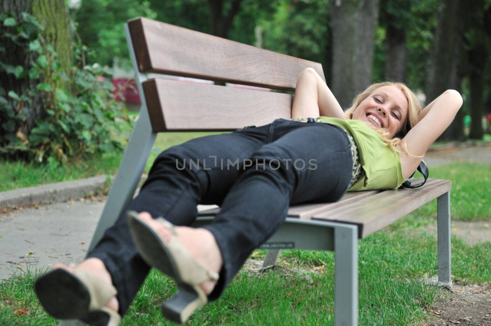 Lifestyle shot of young beautiful smiling woman lying on bench in park outside