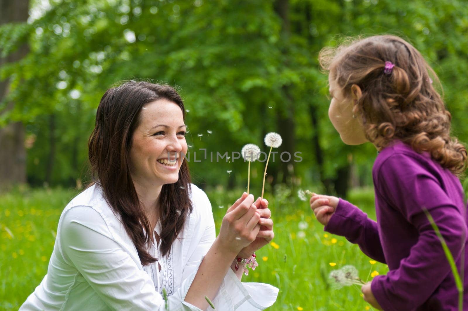 Mother with small daughter blowing to dandelion - lifestyle outdoors scene in park