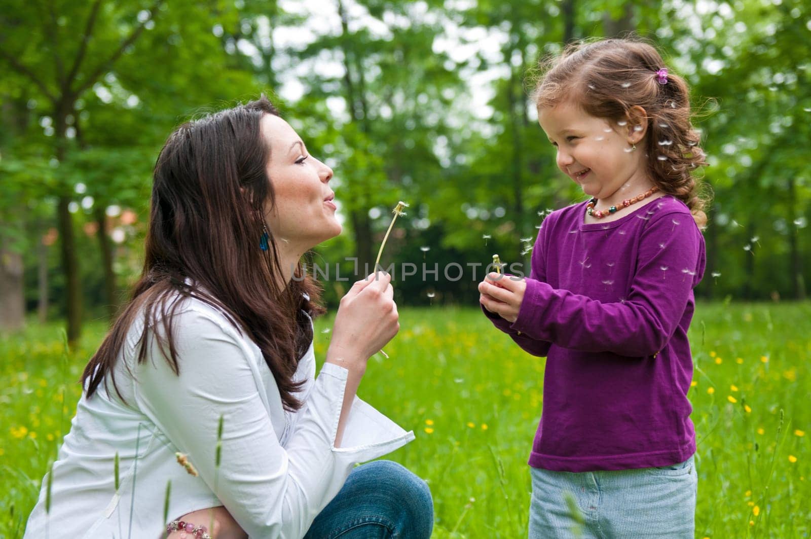 Mother with small daughter blowing to dandelion - lifestyle outdoors scene in park
