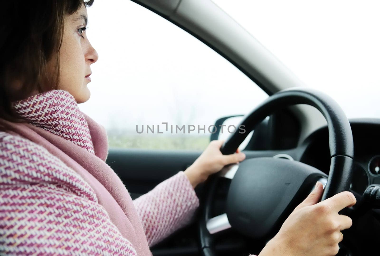 Young business woman driving car in rain (focus on face)