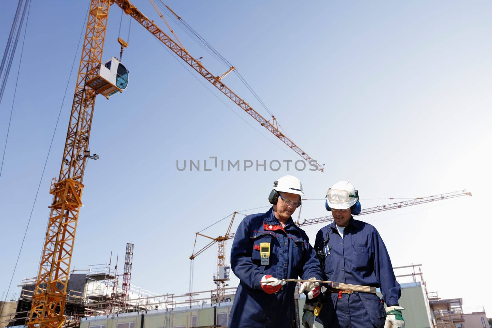 two construction workers inside building site, cranes and scaffoldings in background