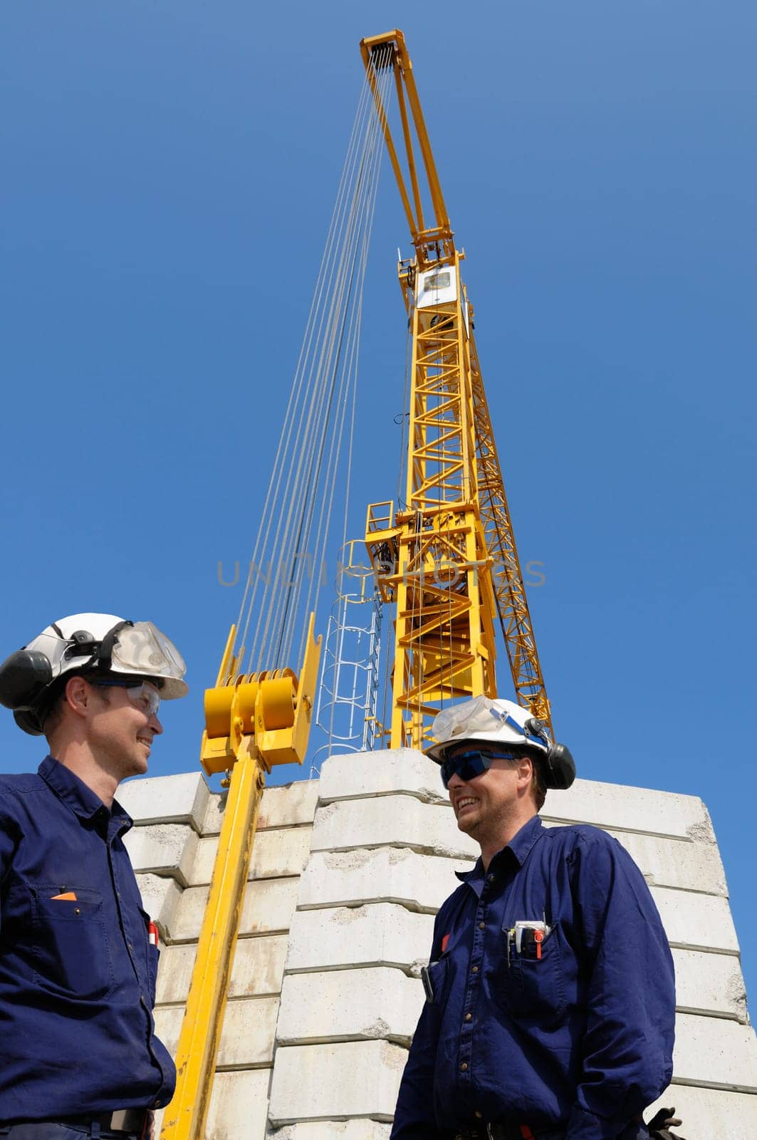 two construction workers with large crane in background