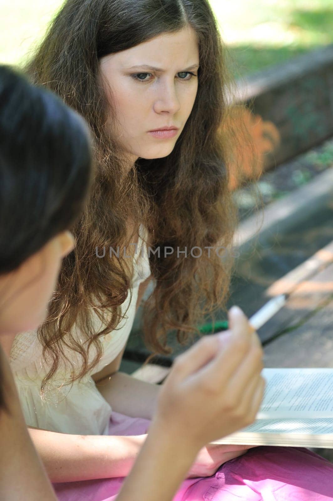Youth culture - two young people outdoors, one woman smoking cigarette annoys and iritates another girl