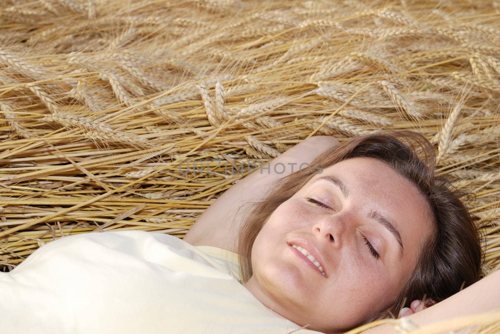 Young cheerful dreaming woman lies in grain with hands under head (copy space in upper part of image)