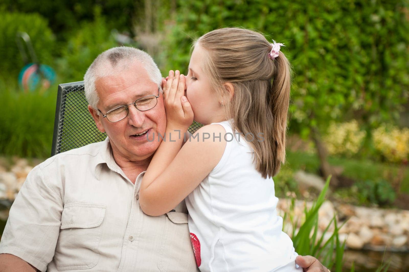 Natural portrait of grandchild whispering to ear of her grandfather in backyard