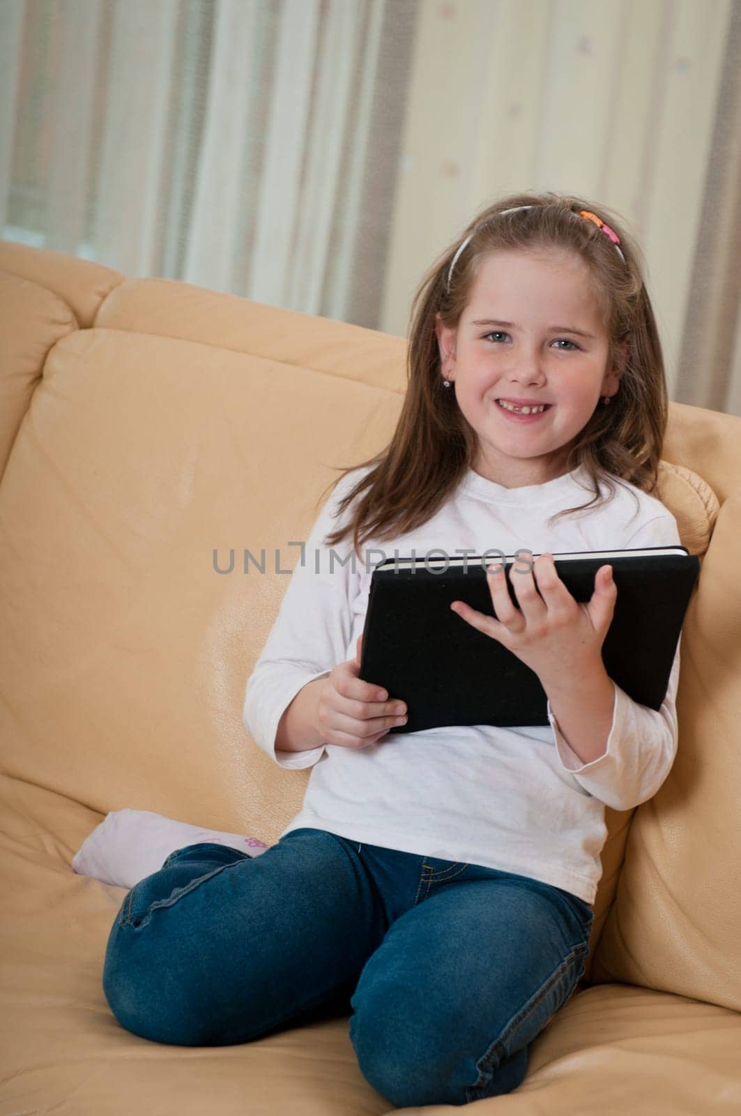 Little child (cute girl) playing with tablet at home sitting on sofa