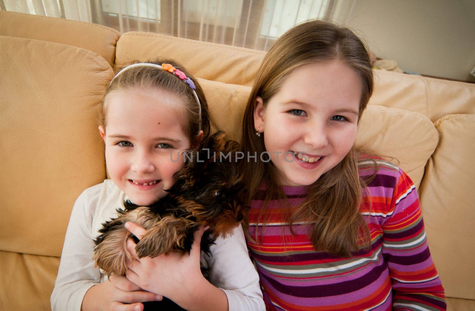 Portrait of smiling cute children (sisters) at home sitting on sofa with their dog
