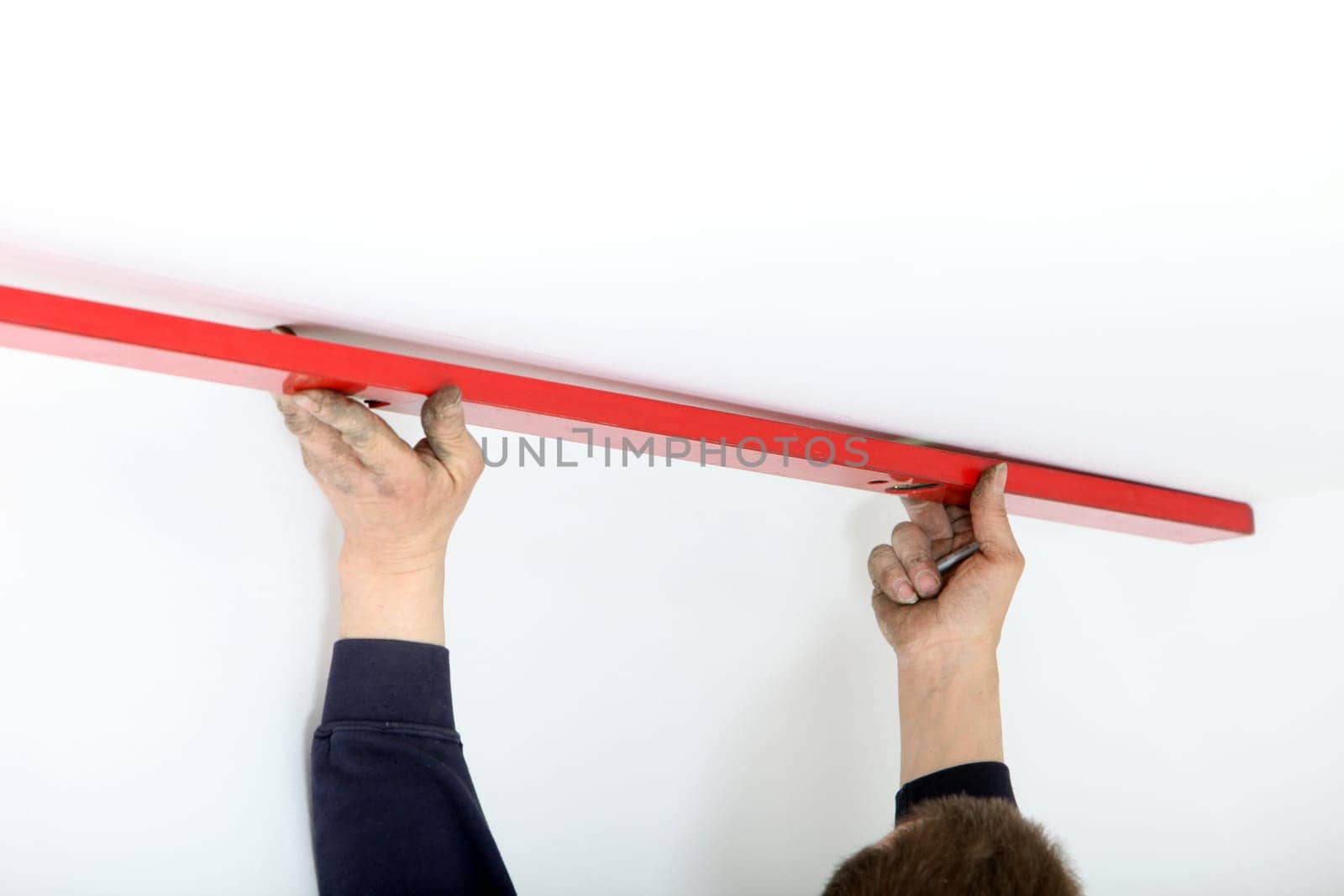 Arms of a man holding a red metal mason&#039 s spirit level to the ceiling during DIY renovations