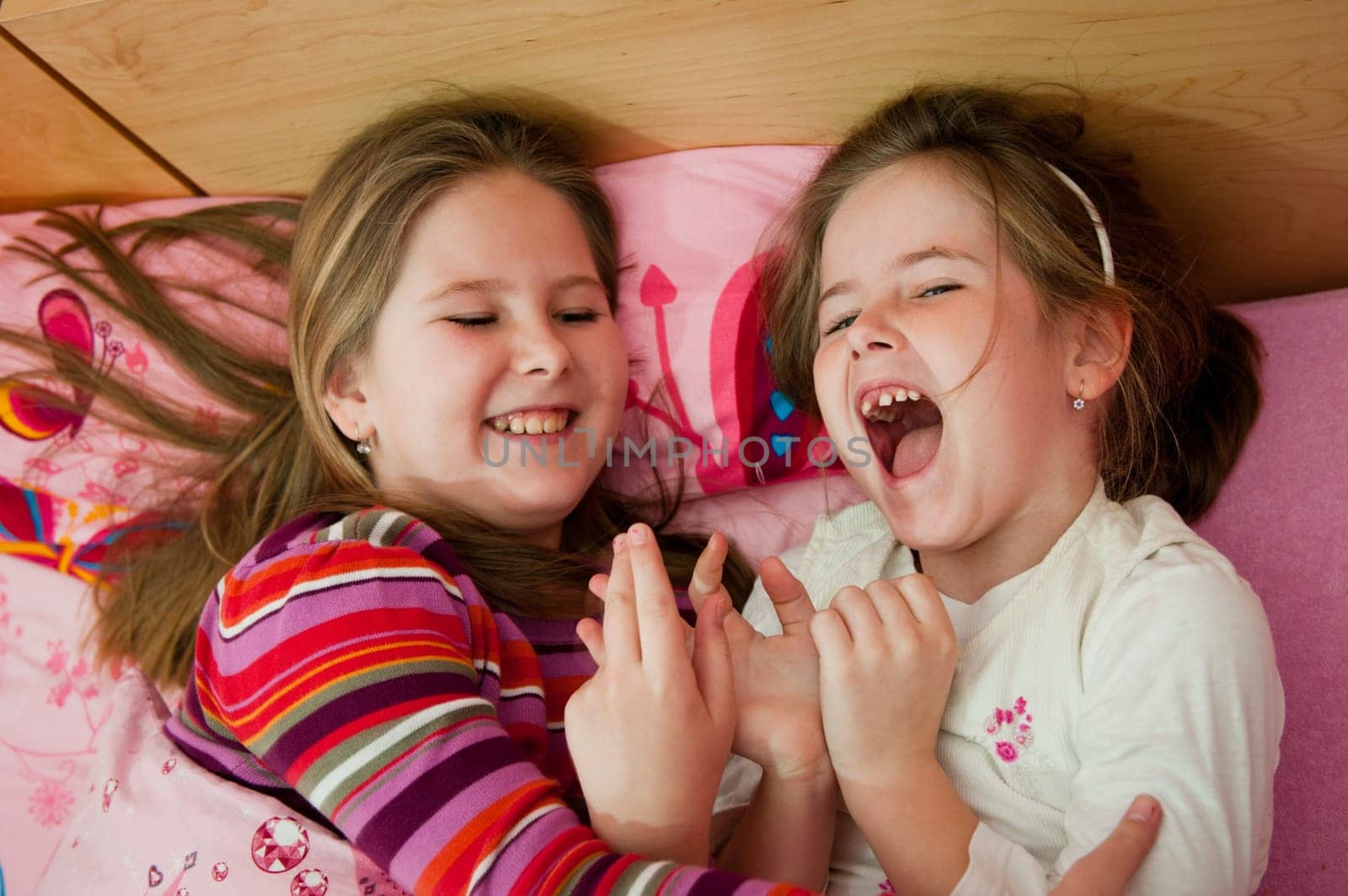 Cute children (two sisters) laughing at home lying in bed