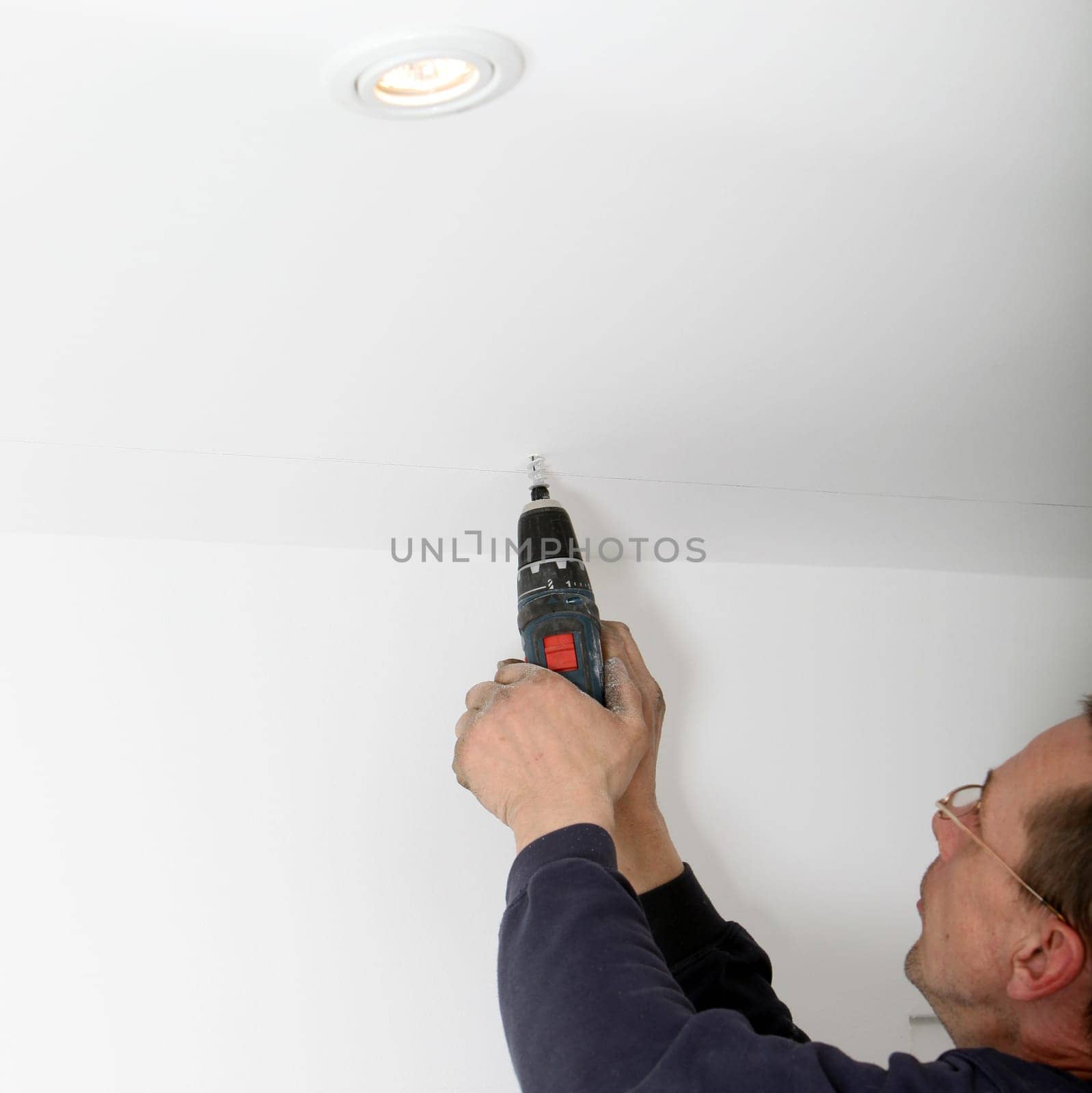 Man using a portable power drill to drill a hole in a white painted ceiling