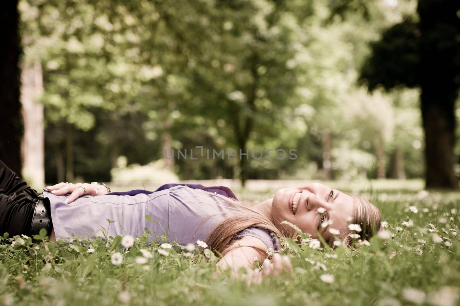 Detail of young woman lying in fresh green grass with flowers - low angle view