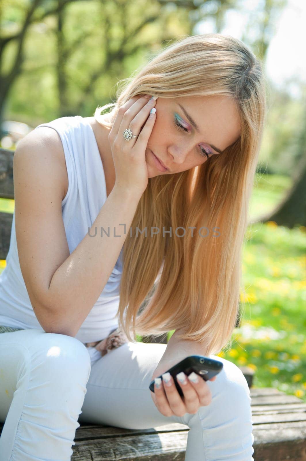 Young worried teen person with unhappy expression holding mobile phone - outdoors in park
