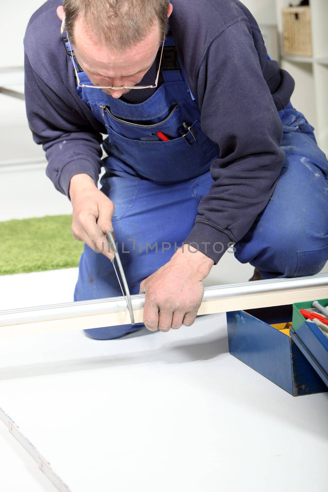 Middle-aged man kneeling on the ground using a hacksaw to shorten a length of metal track