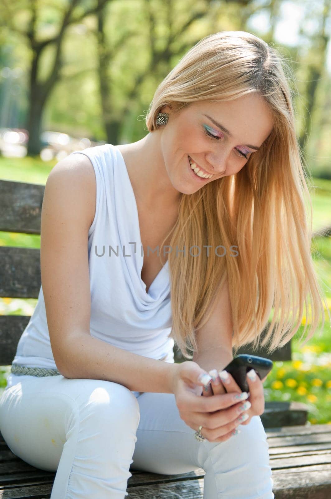 Smiling teen person with mobile phone sitting outdoors on bench