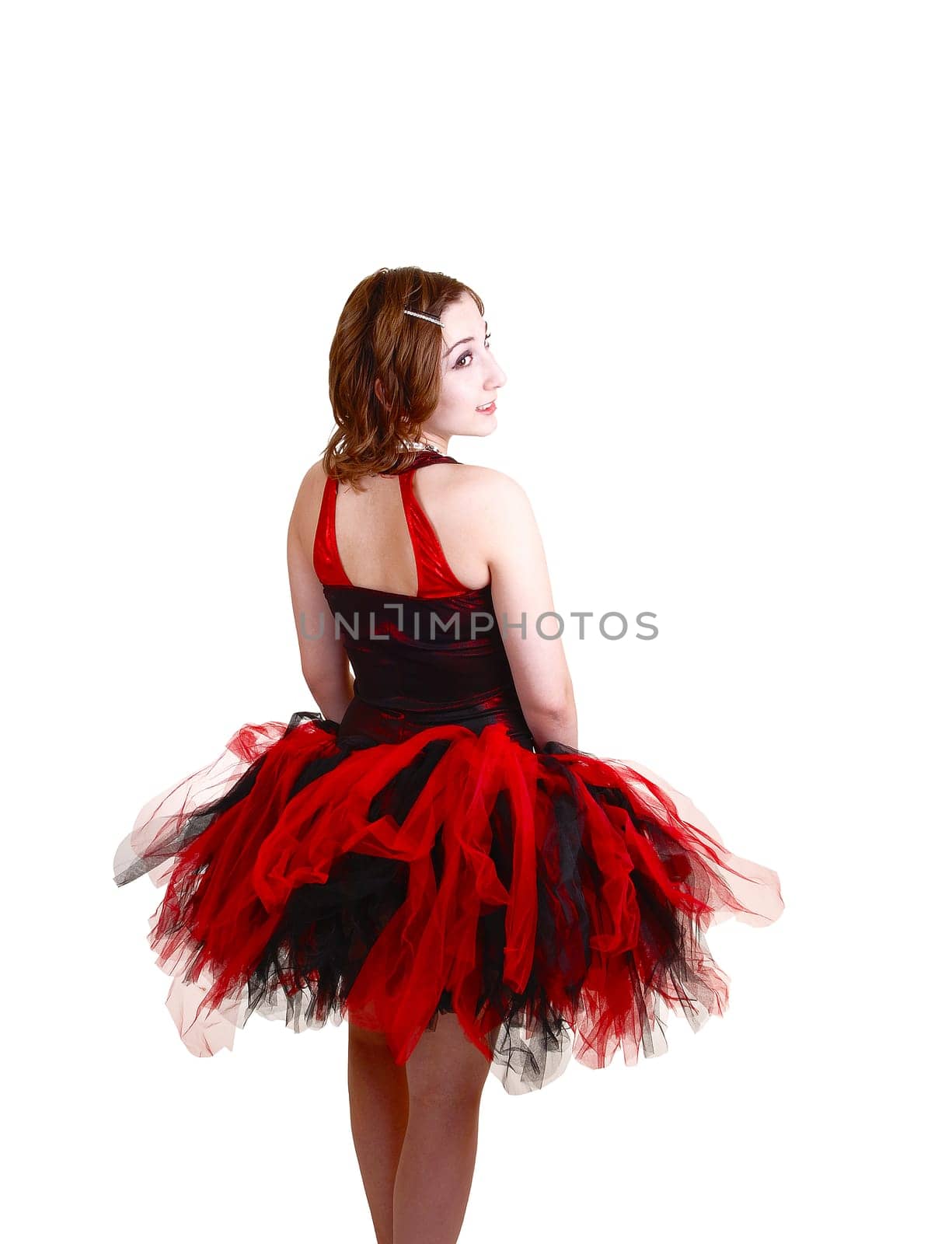 A young teenager ballerina in a red and black dress with a big twill skirt standing from the back in the studio for white background.