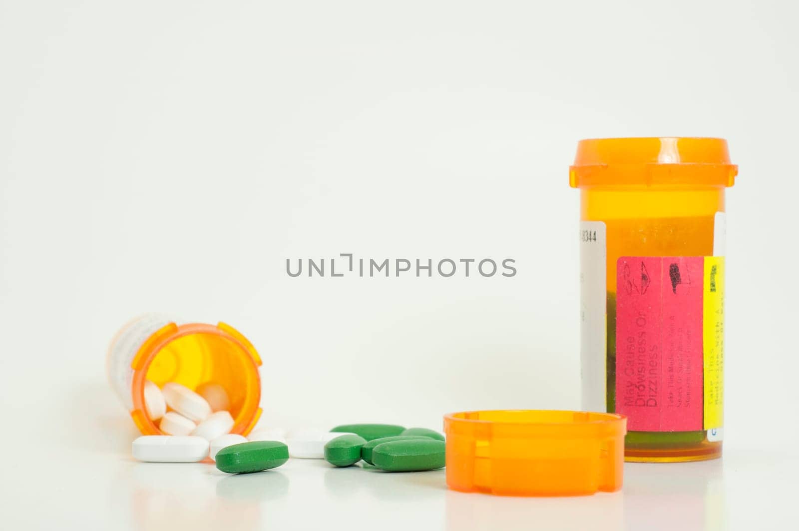spilled white and green prescription pills with two bottles and a lid in foreground