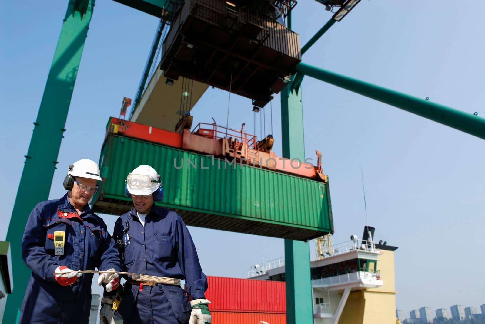 two port-workers with large crane hoisting containers in background